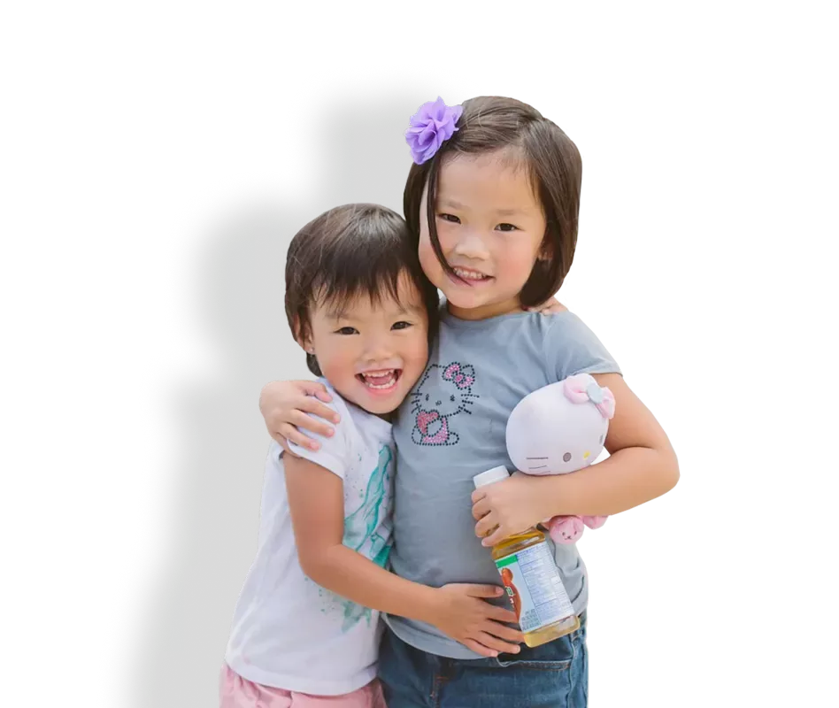 Two young Asian American sisters hugging, smiling looking at the camera